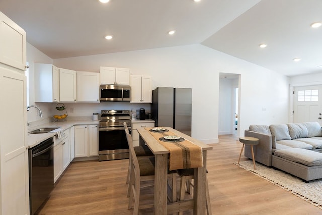 kitchen with lofted ceiling, stainless steel appliances, light wood-type flooring, white cabinetry, and a sink