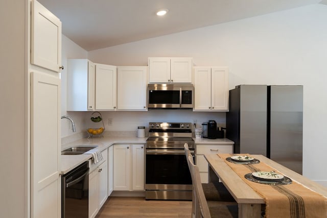 kitchen with vaulted ceiling, stainless steel appliances, light countertops, white cabinetry, and a sink