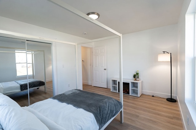 bedroom featuring light wood-type flooring, baseboards, and a closet