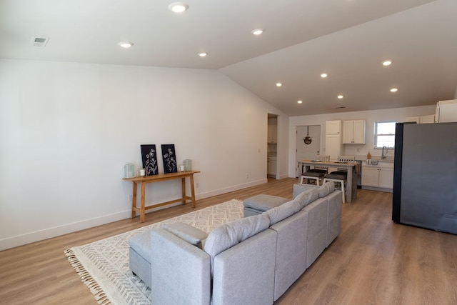 living area with lofted ceiling, light wood-type flooring, visible vents, and baseboards