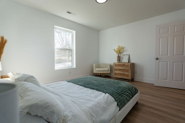 bedroom with baseboards, visible vents, and wood finished floors