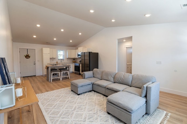 living area with vaulted ceiling, light wood finished floors, visible vents, and baseboards