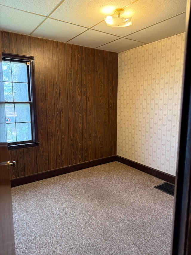 carpeted spare room with visible vents and wood walls