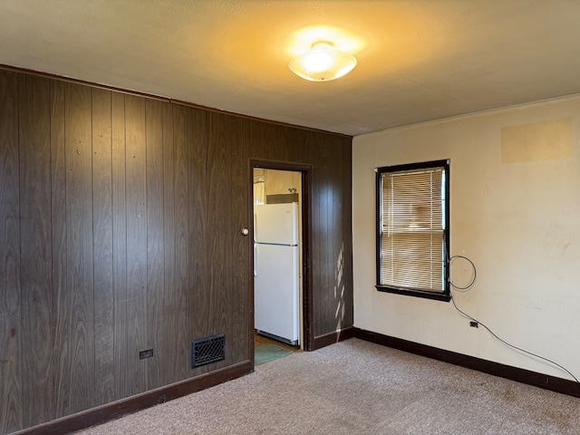 spare room featuring carpet floors, visible vents, wood walls, and baseboards