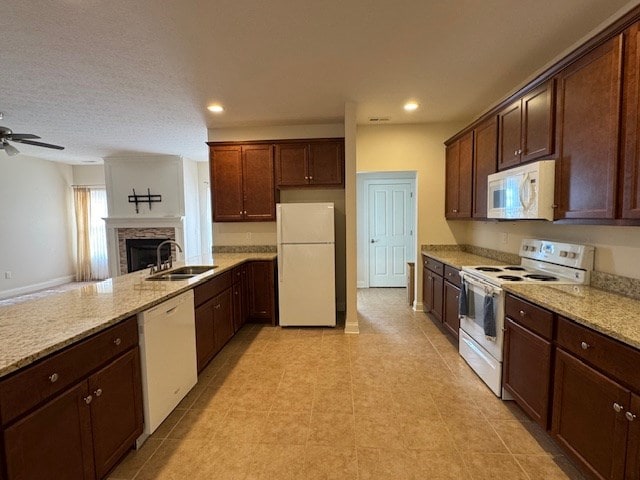 kitchen with ceiling fan, sink, light stone counters, white appliances, and a fireplace