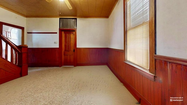 carpeted spare room featuring ornamental molding, wooden ceiling, ceiling fan, and a healthy amount of sunlight