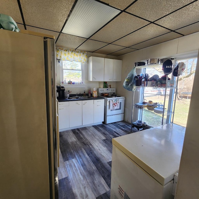 kitchen with white electric stove, a drop ceiling, white cabinetry, and freestanding refrigerator