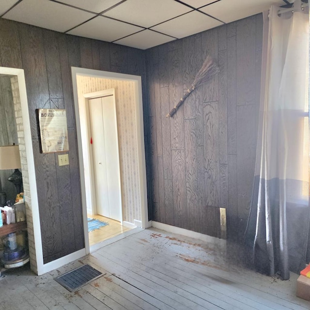 unfurnished room featuring hardwood / wood-style flooring, wooden walls, baseboards, and a drop ceiling