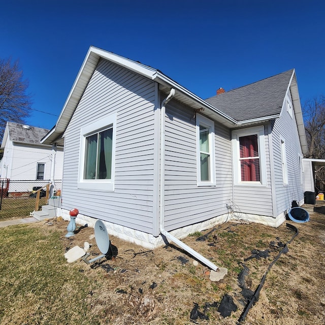 view of property exterior featuring a lawn, roof with shingles, and fence