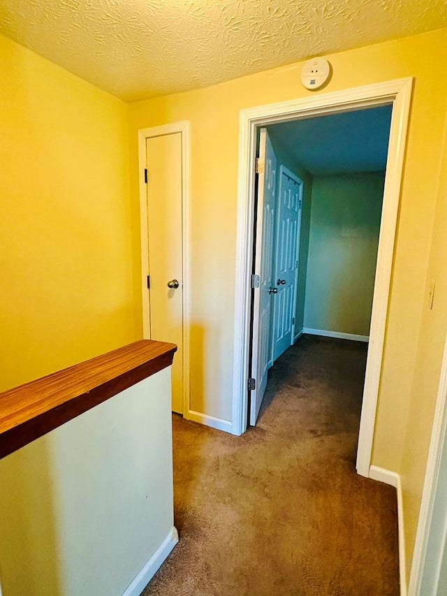 hall featuring dark carpet and a textured ceiling