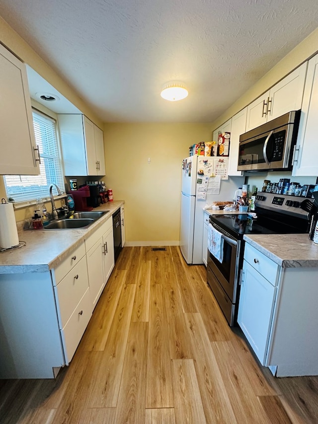 kitchen with a textured ceiling, stainless steel appliances, sink, light hardwood / wood-style flooring, and white cabinets