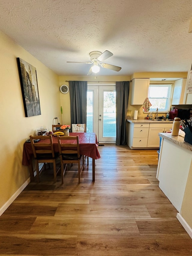 dining space featuring french doors, light wood-type flooring, a textured ceiling, ceiling fan, and sink