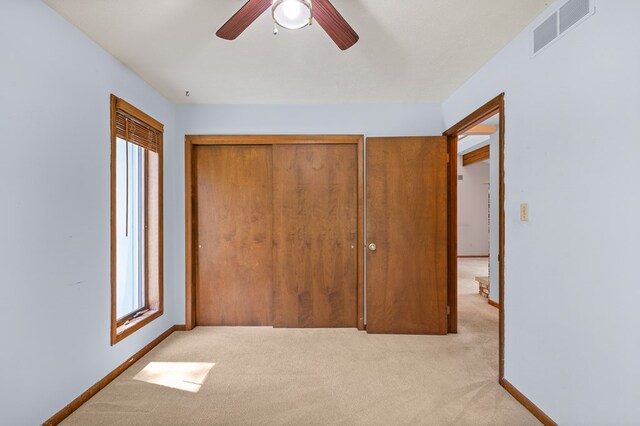 unfurnished bedroom with visible vents, a closet, light carpet, baseboards, and ceiling fan