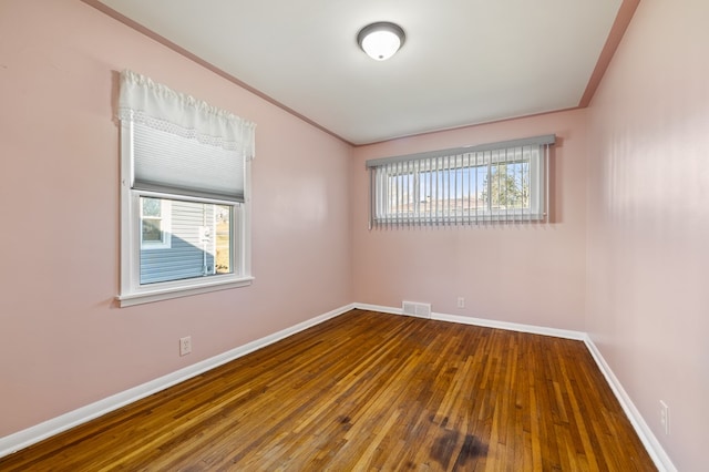 unfurnished room featuring hardwood / wood-style floors, baseboards, visible vents, and a wealth of natural light