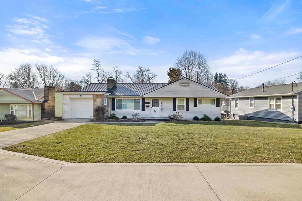 ranch-style house with a standing seam roof, an attached garage, concrete driveway, a front lawn, and metal roof