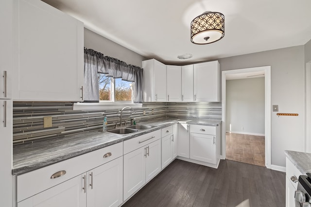 kitchen with a sink, stainless steel range oven, backsplash, dark wood finished floors, and white cabinetry