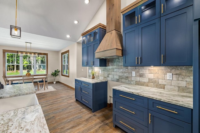 kitchen with blue cabinetry, backsplash, vaulted ceiling, decorative light fixtures, and custom exhaust hood