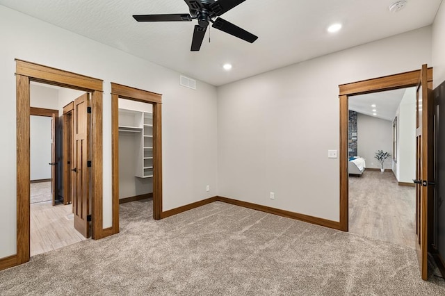 unfurnished bedroom with ceiling fan, a walk in closet, light carpet, and a closet