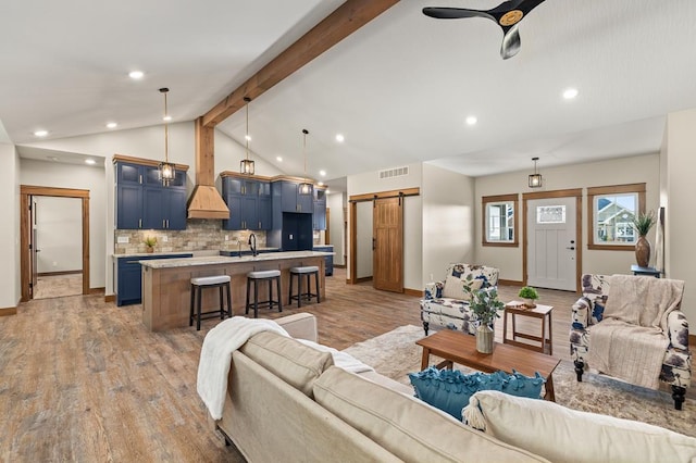 living room featuring hardwood / wood-style floors, lofted ceiling with beams, sink, ceiling fan, and a barn door