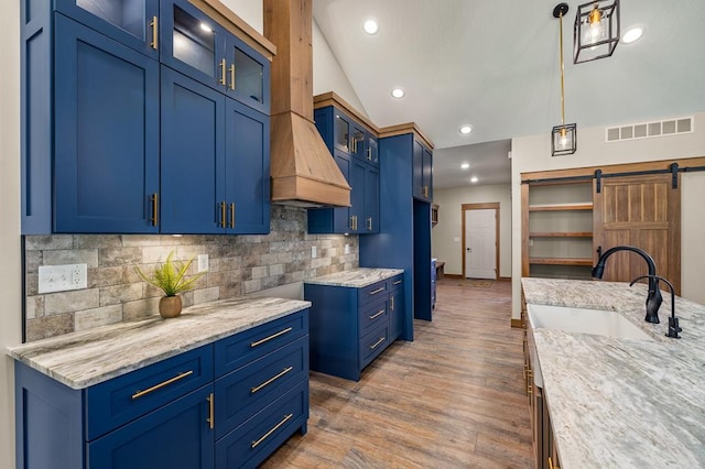 kitchen with pendant lighting, blue cabinets, a barn door, light stone countertops, and wood-type flooring