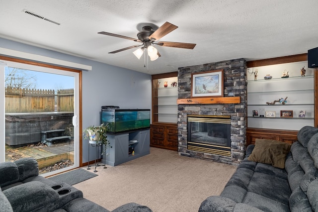 carpeted living room featuring ceiling fan, a stone fireplace, and a textured ceiling