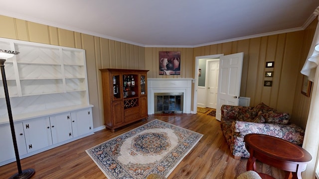 living area featuring a fireplace with flush hearth, crown molding, and wood finished floors