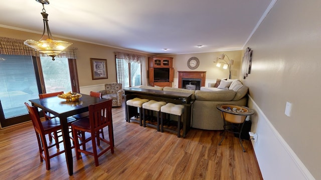 dining room featuring a fireplace, crown molding, baseboards, and wood finished floors
