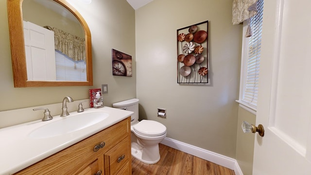 half bath featuring vanity, toilet, baseboards, and wood finished floors
