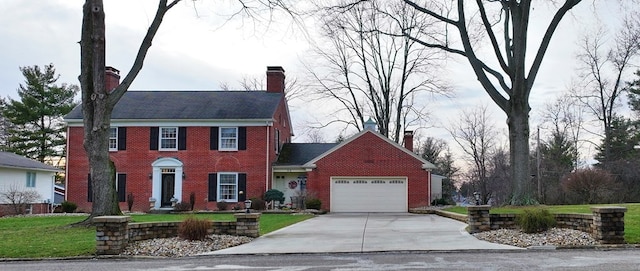 colonial home featuring an attached garage, a chimney, a front lawn, brick siding, and driveway