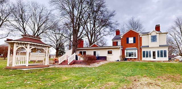 rear view of property with a gazebo, a chimney, and a lawn