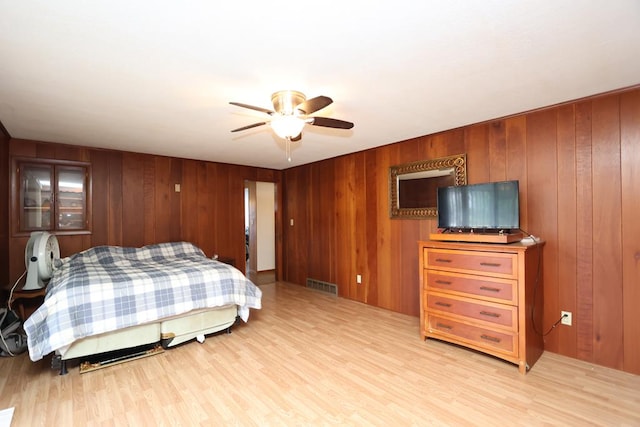 bedroom with ceiling fan, visible vents, light wood-style floors, and wooden walls