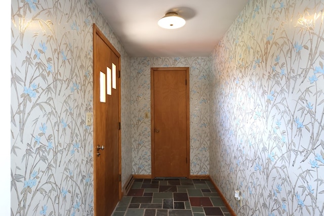 corridor featuring wallpapered walls, stone tile flooring, and baseboards