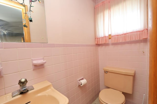 half bathroom with tile walls, ceiling fan, a sink, and toilet