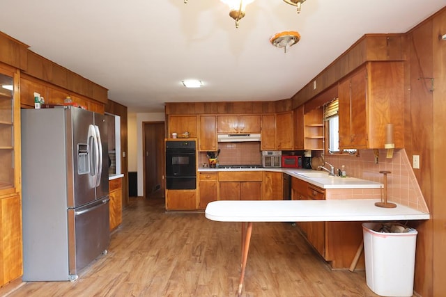 kitchen featuring light wood finished floors, oven, under cabinet range hood, stainless steel fridge with ice dispenser, and brown cabinetry