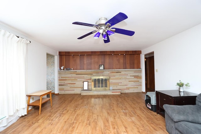 living room with light wood-style flooring, an accent wall, a glass covered fireplace, and a ceiling fan
