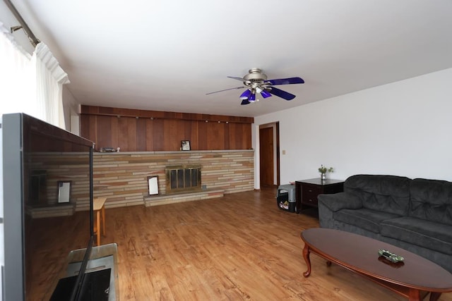 living room featuring a ceiling fan, a stone fireplace, and light wood finished floors