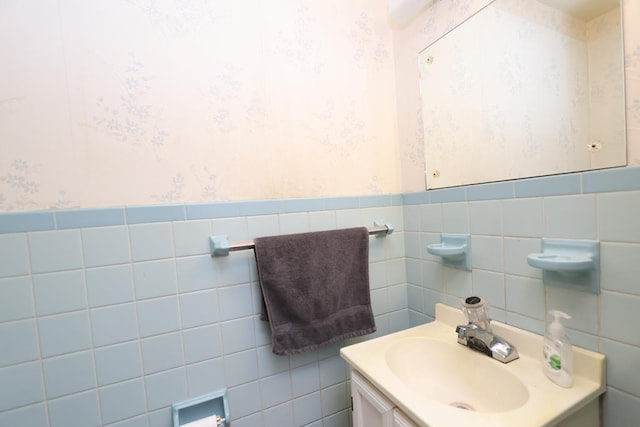 bathroom with wallpapered walls, vanity, tile walls, and wainscoting