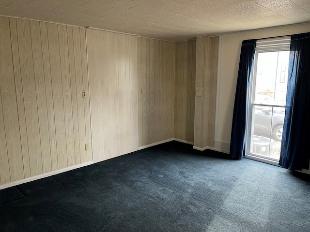 unfurnished room featuring wood walls and dark colored carpet