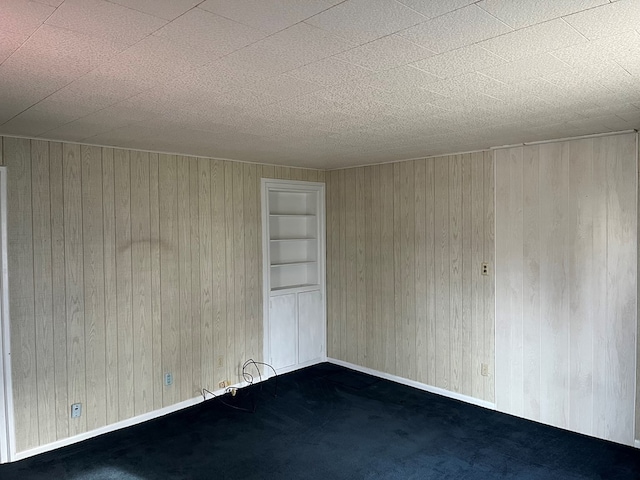 spare room featuring dark carpet, built in features, and wood walls