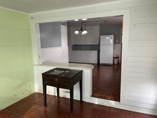 kitchen with a notable chandelier, ornamental molding, decorative light fixtures, kitchen peninsula, and white fridge