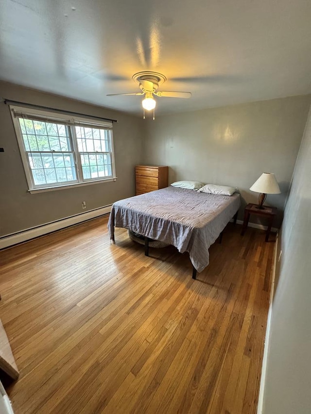 bedroom with a ceiling fan, baseboard heating, and hardwood / wood-style flooring