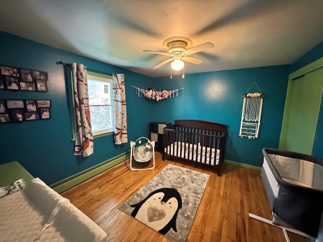 bedroom with a baseboard heating unit, a ceiling fan, wood finished floors, and baseboards