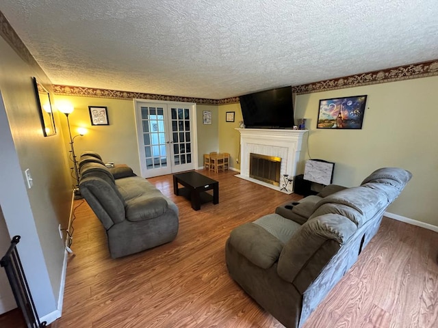 living room featuring a textured ceiling, french doors, baseboards, a tile fireplace, and wood finished floors