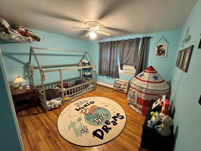 bedroom with baseboard heating, wood finished floors, and a ceiling fan