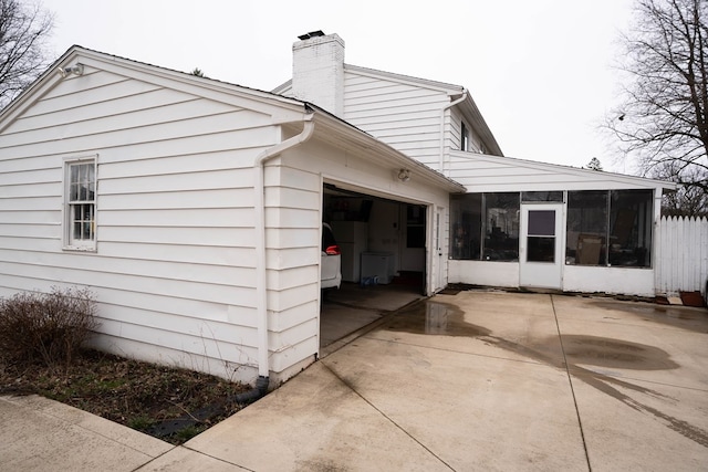 view of home's exterior featuring an attached garage, driveway, a chimney, and a sunroom