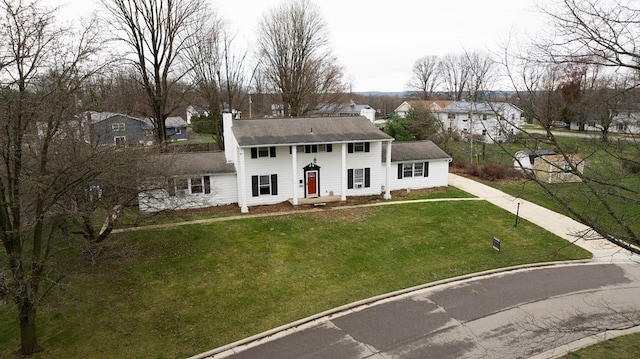 colonial inspired home with driveway, a residential view, a chimney, roof with shingles, and a front yard
