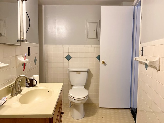 bathroom featuring electric panel, vanity, tile walls, and toilet