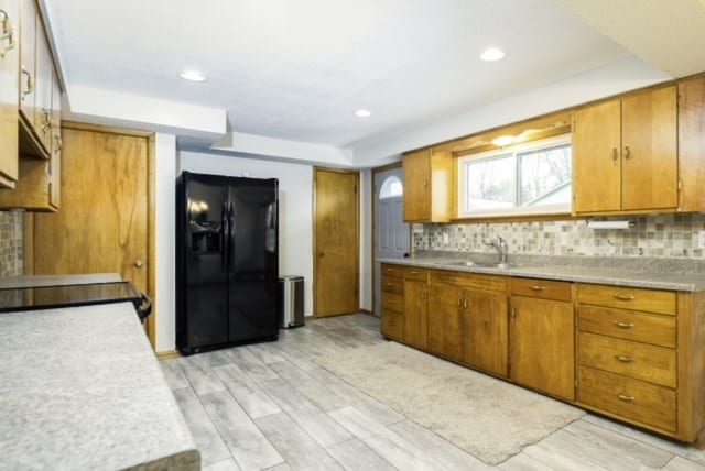 kitchen featuring stove, black fridge, sink, light hardwood / wood-style flooring, and tasteful backsplash