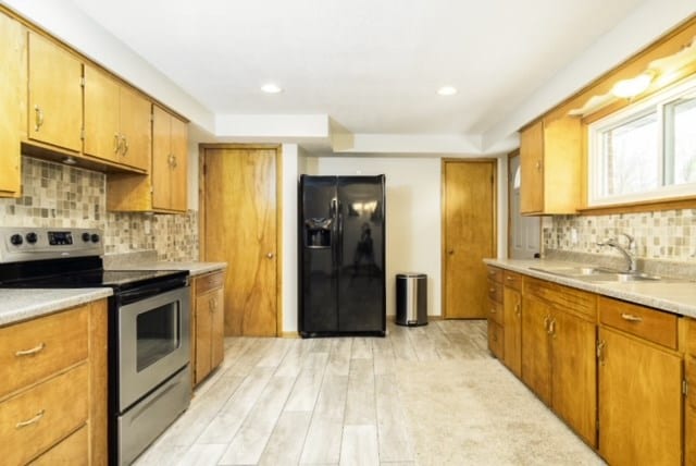 kitchen featuring backsplash, black fridge, sink, electric range, and light hardwood / wood-style floors