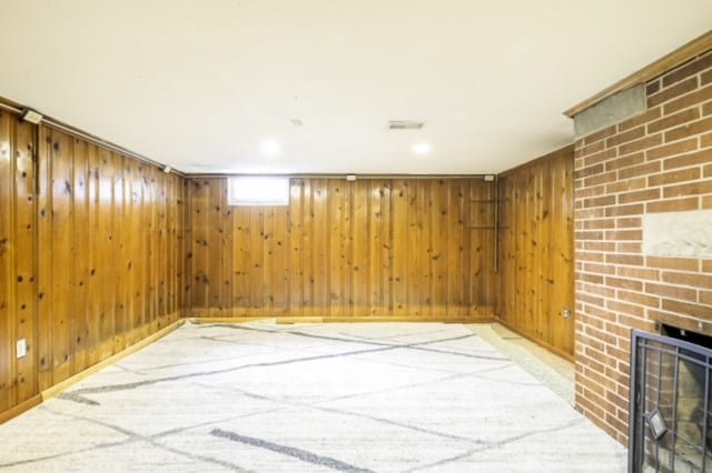 basement with light carpet, wooden walls, and a brick fireplace